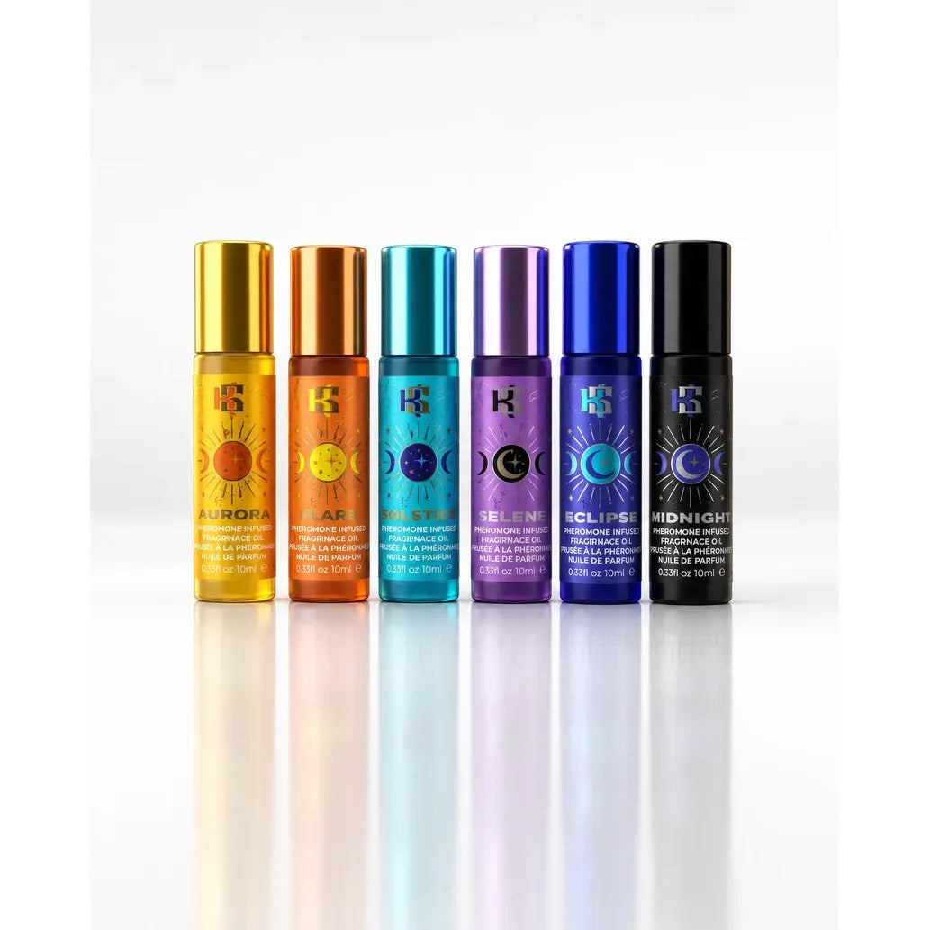 Six small cylindrical perfume or fragrance oil bottles with metallic caps are lined up on a white reflective surface against a white background. The bottles are labeled with colorful sun and moon symbols and names including Aurora, Apollo, Selene, Eclipse, Midnight, and Luna.