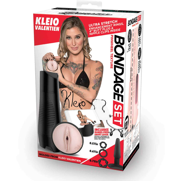Red and white packaging with Kleio posed in a black bra. Next to her is the beige male masturbator with a vaginal opening and a black hard shell, a black anal plug, three black cockrings, silver and black nipple clamps, and a black cell phone stand