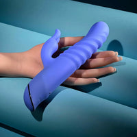A blue silicone personal massager with a ribbed shaft and curved base, shown being held by a hand against a teal background.