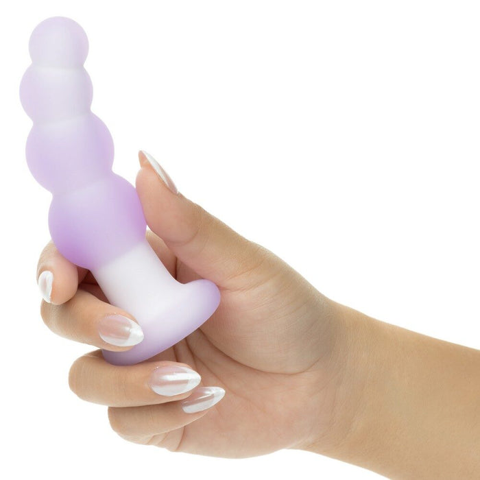Hand holding a purple and white silicone anal plug on a white background