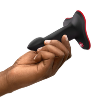 Hand holding a black and red limba flex s dildo device on a white background