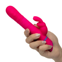 A hand holding a bright pink silicone personal massager with a ribbed shaft and a curved, finger-like suction or stimulation tip, shown against a plain white background.