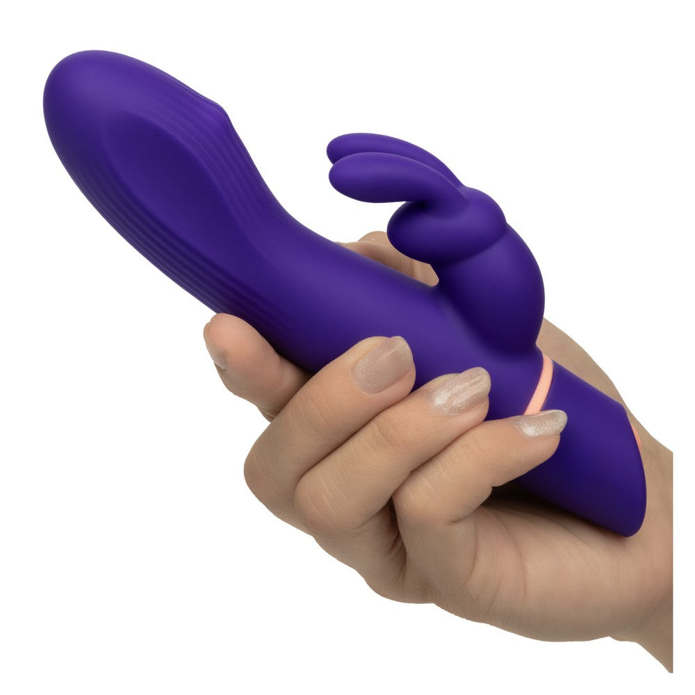 A hand holding a purple rabbit-shaped silicone vibrator against a plain white background.