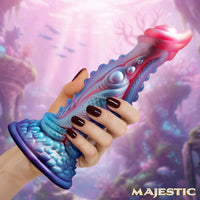 Colorful dildo with a hand holding it against a fantasy-themed background, featuring the brand 'Majestic'.