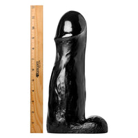 Black silicone dildo next to a ruler on a white background