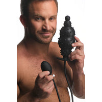 A person holding an inflatable anal plug with a textured surface and a pump attached via a hose.