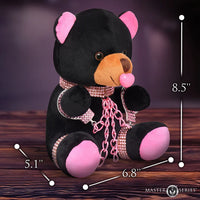 Black teddy bear with pink accents and measurements on a wooden surface
