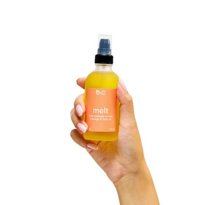 Hand holding a bottle of D:C 'melt' massage and bath oil against a white background
