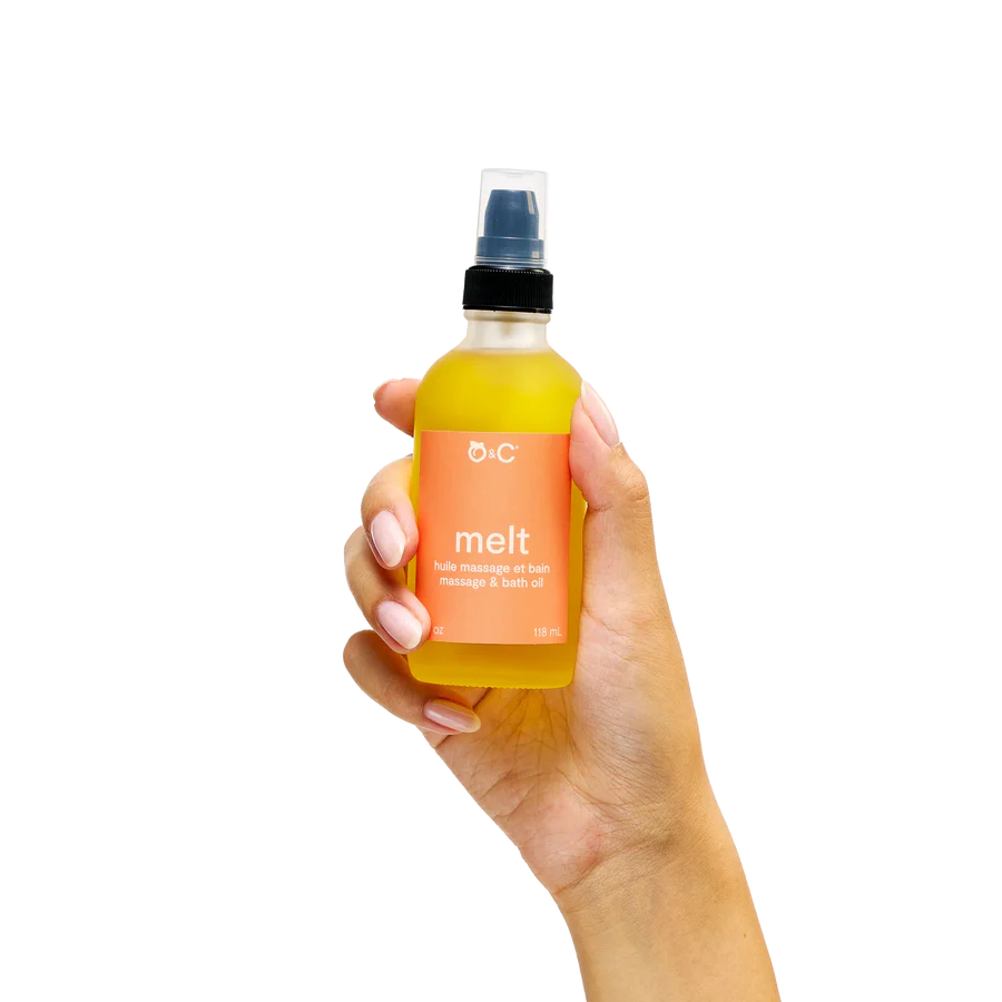 Hand holding a bottle of D:C 'melt' massage and bath oil against a white background