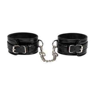 Pair of black leather cuffs with a chain on a white background