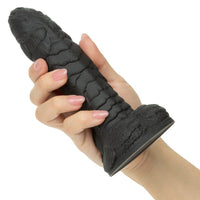 Hand holding a textured black gill man dildo against a white background
