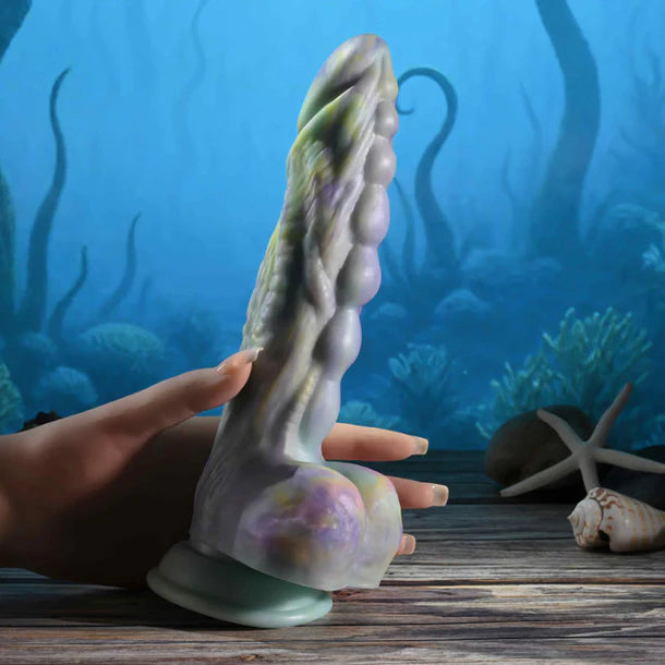 monsters ball dildo with balls with a hand holding it against an underwater-themed background.