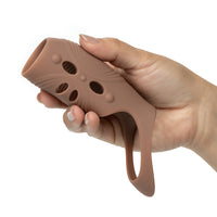 A hand holding a brown silicone penis extentions against a plain white background.