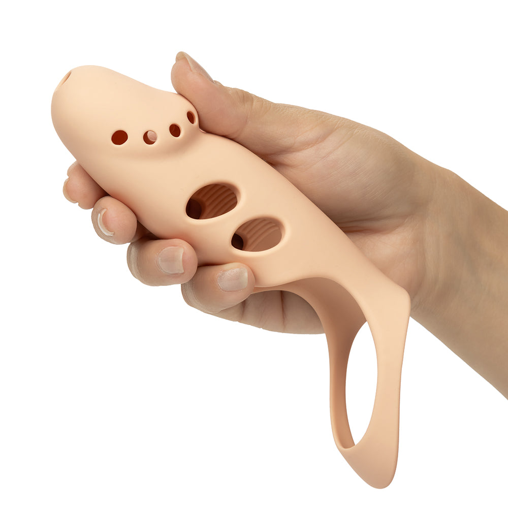 A hand holding a beige silicone penis extension against a plain white background.