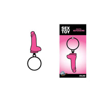 The image features the "Glitter Dildo" Metal Keychain by Wood Rocket, which is pink and has a sparkling, playful design. It is displayed both on its own and in packaging that includes a stylish 5" x 2.