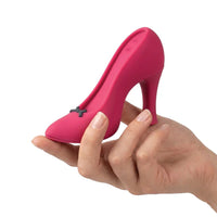 A hand holding a small, bright pink high-heeled shoe-shaped object with a tiny dark bow detail, photographed against a plain white background.