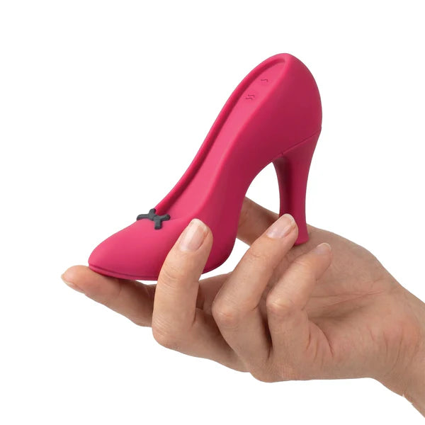A hand holding a small, bright pink high-heeled shoe-shaped object with a tiny dark bow detail, photographed against a plain white background.