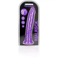 a glow in the dark purple penis shaped dildo with a suction cup base shown in its plastic packaging