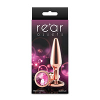 Package of a rose gold butt plug with pink gem, branded 'rear assets', on a white background.