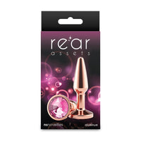 Package of a rose gold butt plug with pink gem on a purple background, branded 'rear assets'.