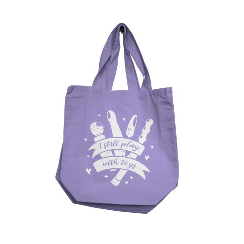 Purple tote bag with i still play with toys in white text and graphics on a white background