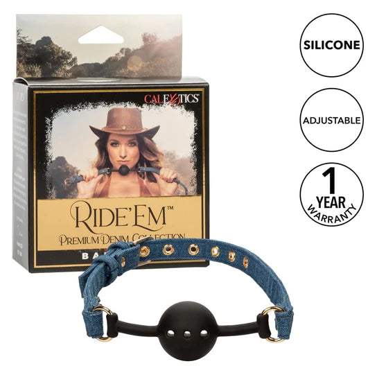 a black ball gag with air holes and denim blue straps with gold accents. It is shown next to a display box depicting a cowgirl holding that gag
