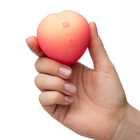 Hand holding a pink peach with 'ROMP' branding on a white background