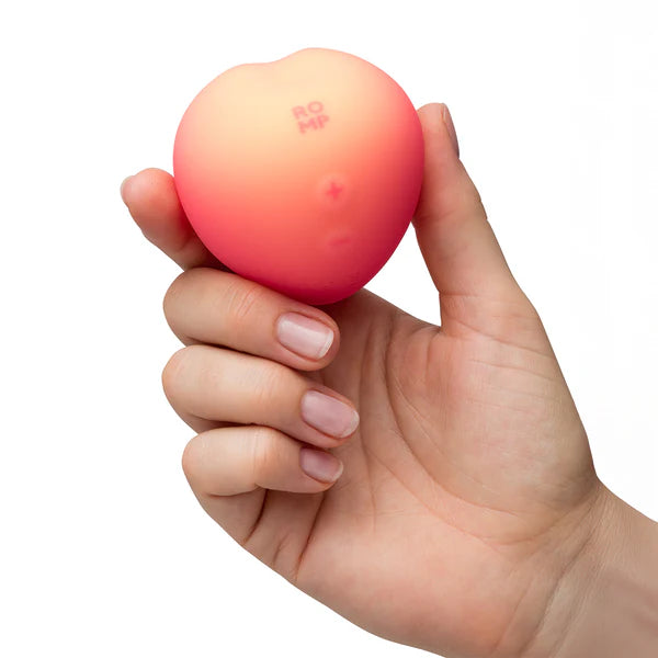Hand holding a pink peach with 'ROMP' branding on a white background