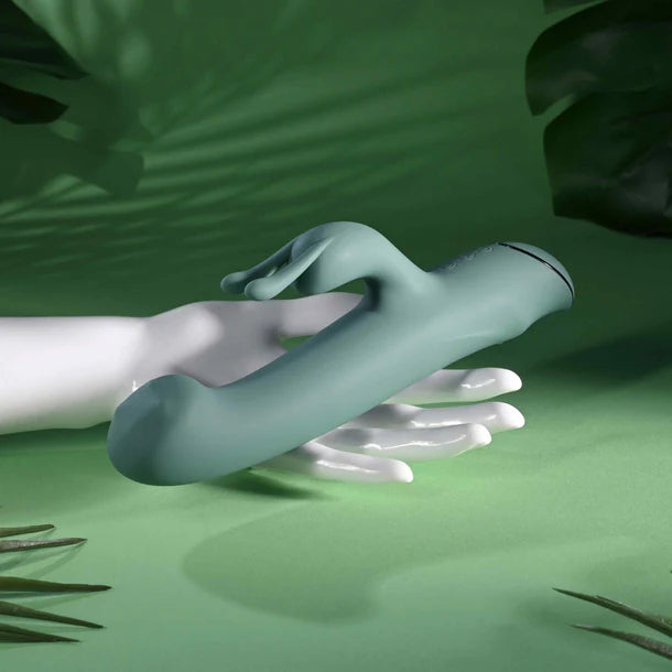 Decorative hand holding a green vibrator against a green background with leaf patterns