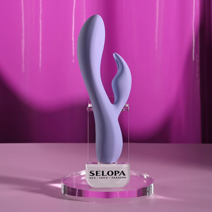 Selopa Purple Craze dual vibrator in purple with curved shaft and flexible stimulator, displayed on a branded stand.