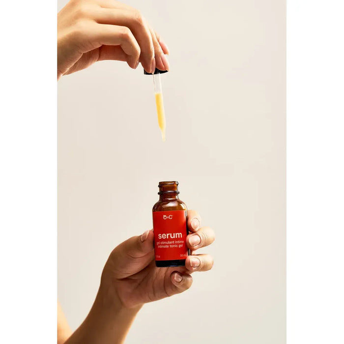 Hand holding a red serum bottle with dropper against a plain background