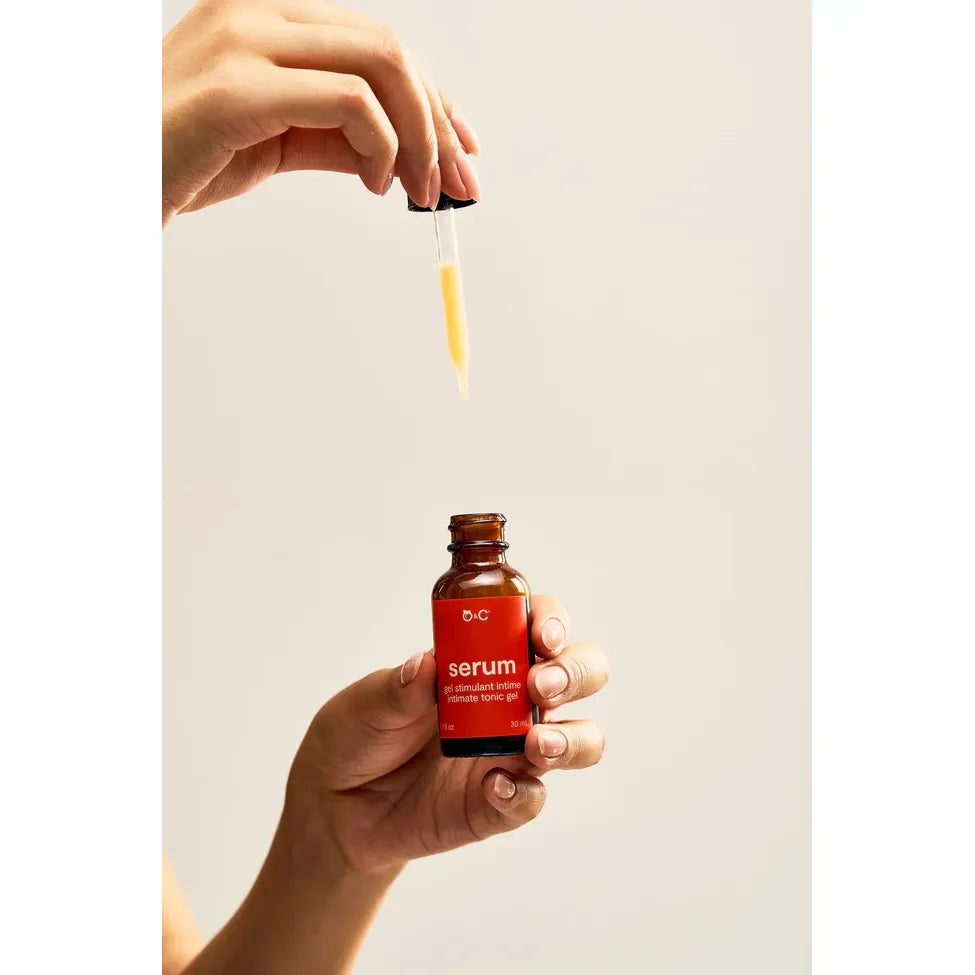 Hand holding a red serum bottle with dropper against a plain background