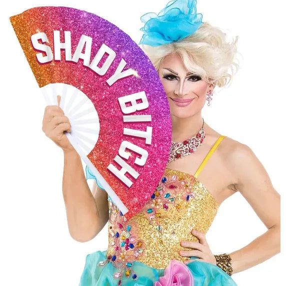 Person in colorful outfit holding a glittery fan with 'SHADY BITCH' text on a white background