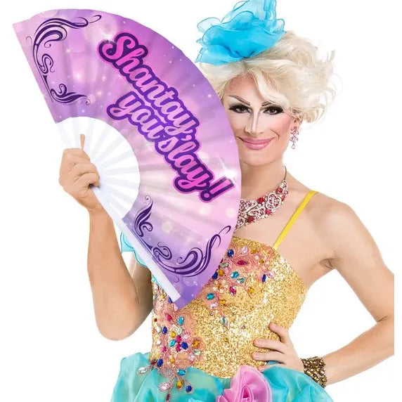 Person in colorful costume holding a fan with 'Shantay you slay!' text on a white background