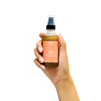Hand holding a bottle of OHC Silk dry massage oil against a white background