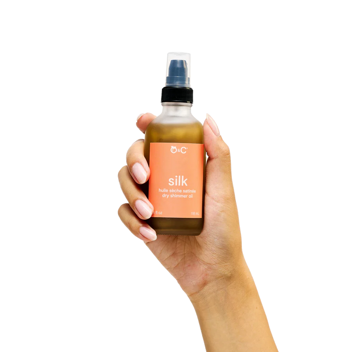 Hand holding a bottle of OHC Silk dry massage oil against a white background
