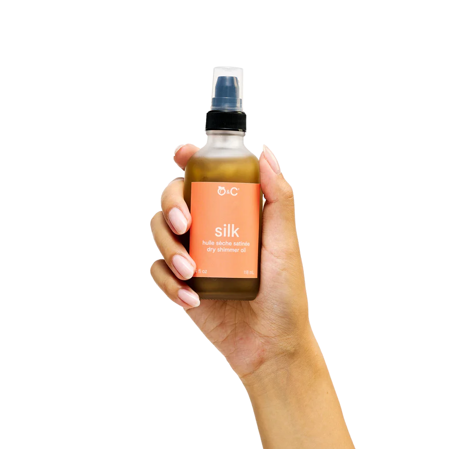 Hand holding a bottle of OHC Silk dry massage oil against a white background