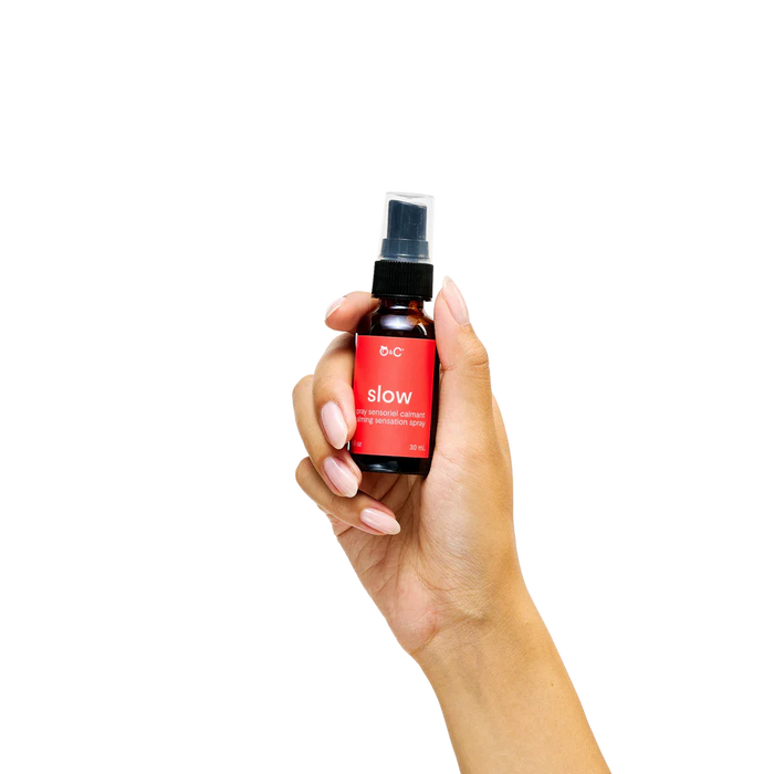 Hand holding a small spray bottle of slow calming with a red label on a white background