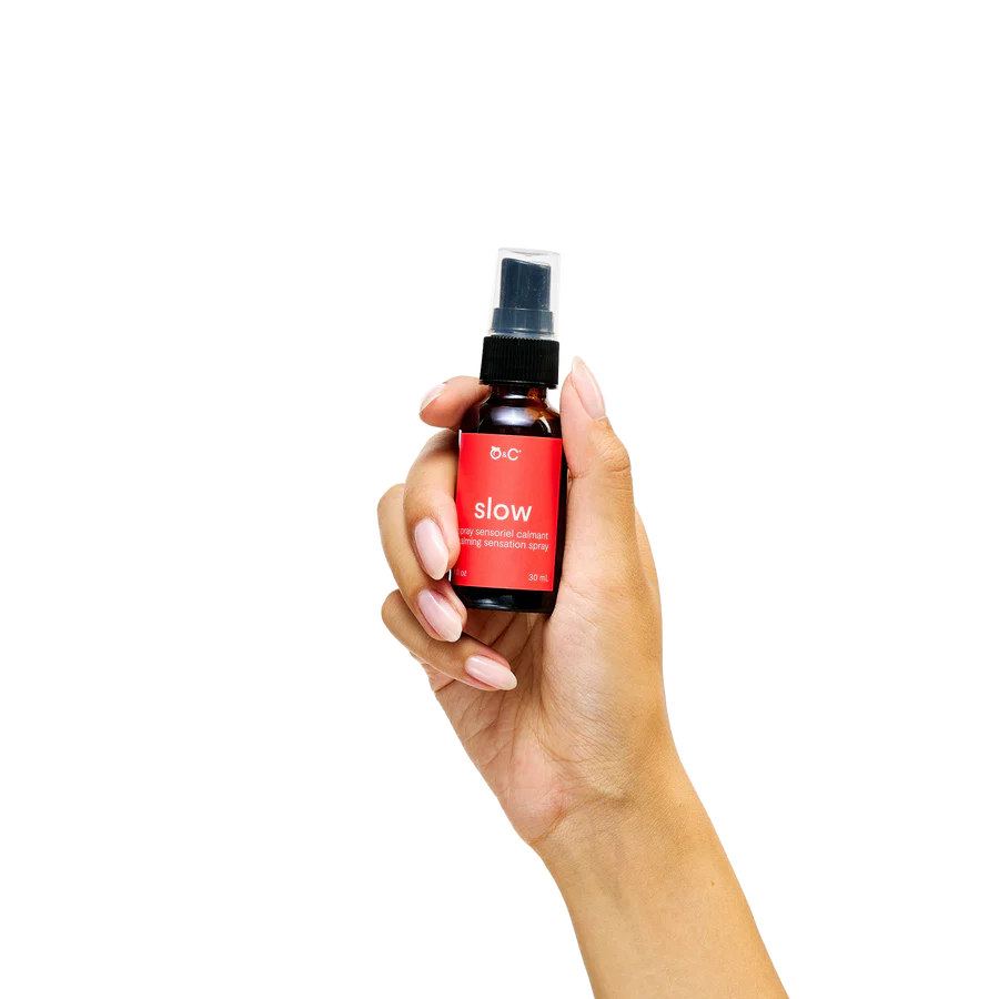 Hand holding a small spray bottle of slow calming with a red label on a white background