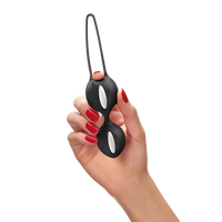 Hand holding a black and white duo kegel balls with a strap on a white background
