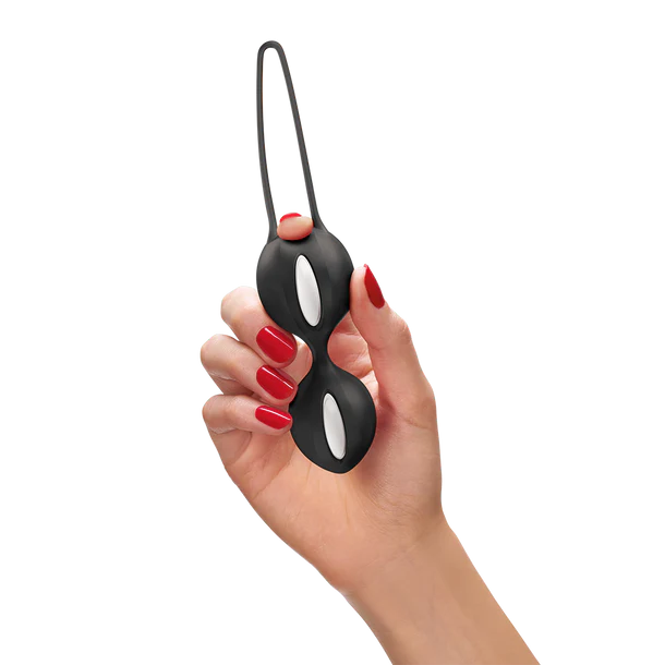 Hand holding a black and white duo kegel balls with a strap on a white background