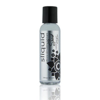 The product comes in a clear bottle with a black cap. It has a silver label with black writing and a black flower design