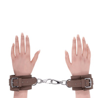 2 hands wearing brown handcuffs on wrists