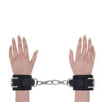 Black faux-leather wrist cuffs with silver metal buckles and a connecting silver spring ring clasp, shown on two mannequin hands against a plain white background.