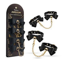 Temptasia Ardor Bow Wrist and Ankle Restraint Set by Blush featuring adjustable black cuffs with decorative bows and gold-tone chain connectors, shown alongside retail packaging.
