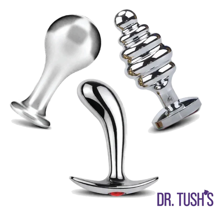 Dr. Tush’s Tools of Temptation Collection featuring three polished silver metal anal plugs in Knob, Prostate and Hive shapes with flared bases.