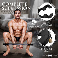 Man sitting on the floor with the 'Complete Submission wrist & ankle stocks' in a bedroom setting.