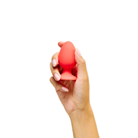 Hand holding a red silicone egg-shaped anal plug product against a white background