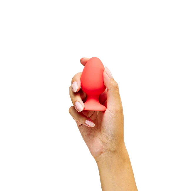Hand holding a red silicone egg-shaped anal plug product against a white background