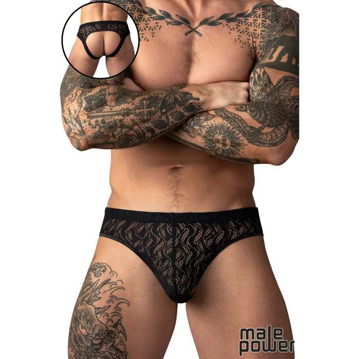 A tattooed male model wearing black lace briefs against a white background, with a circular inset showing a close-up of the back of the underwear.